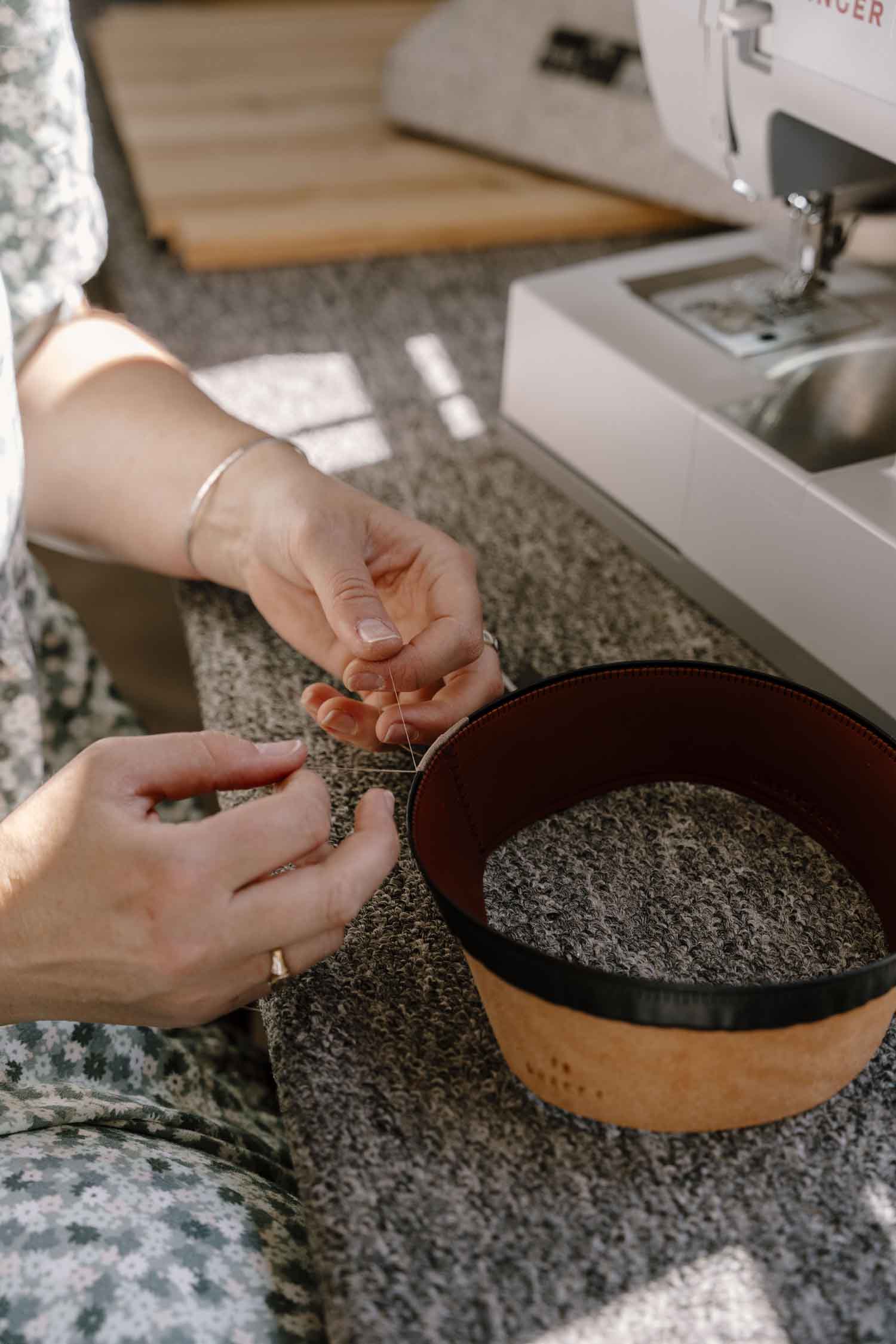 Close-up of Laura Hall’s hands stitching and tying off threads on a leather hat sweatband.