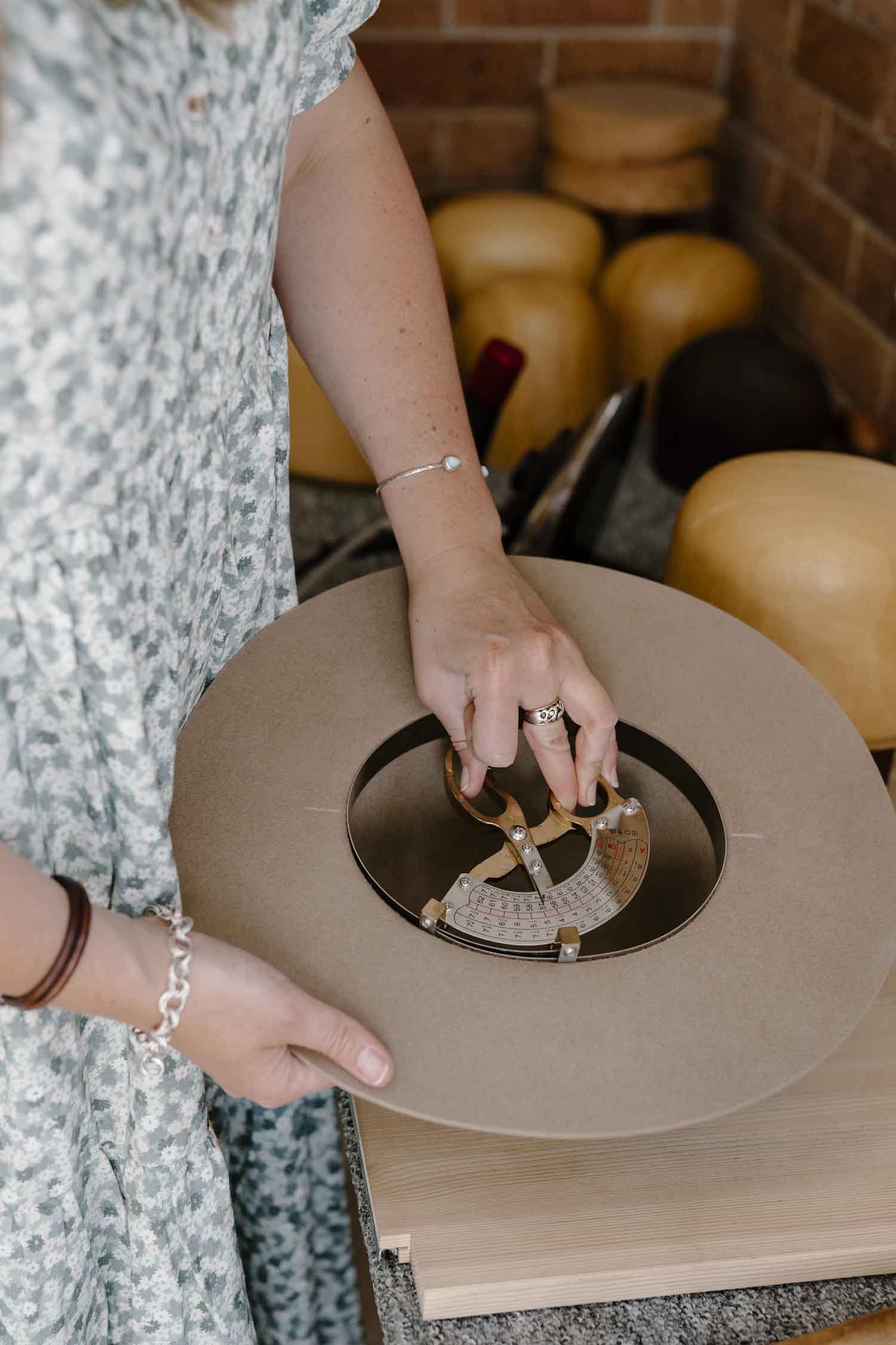 Laura Hall, founder and hatmaker of PHYLLi Designs, measuring a custom hat using a crown sizing tool in her regional Australian studio.