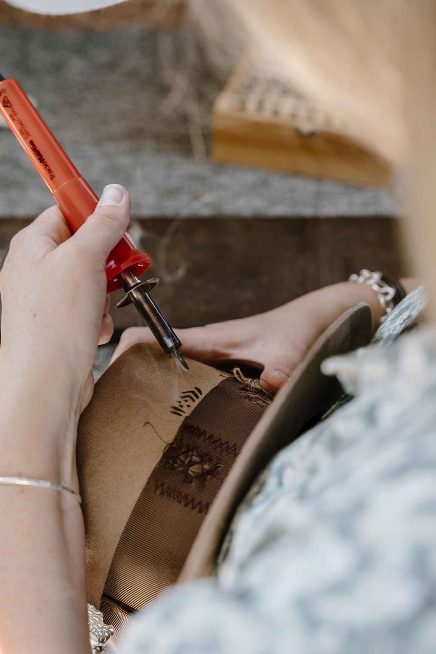 Laura Hall branding pattern details into the back of a felt hat in the PHYLLi Designs studio.