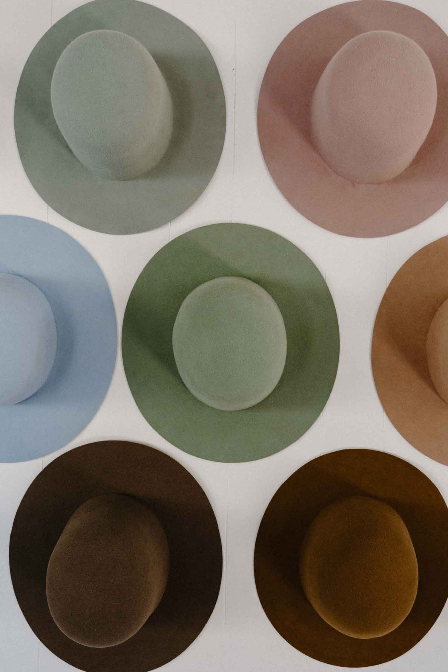 Collection of colourful felt hat bases hanging on a studio wall at PHYLLi Designs.