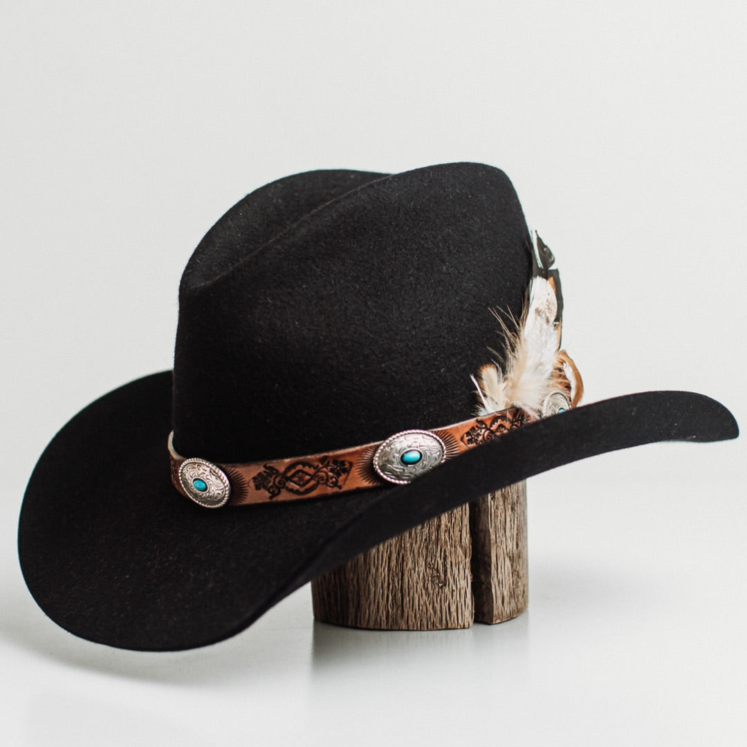 Front left angle of The PHYLLi dark navy felt hat by PHYLLi Designs with Buffalo Girl Rugged Desert tie back band and fallen feather bunch.
