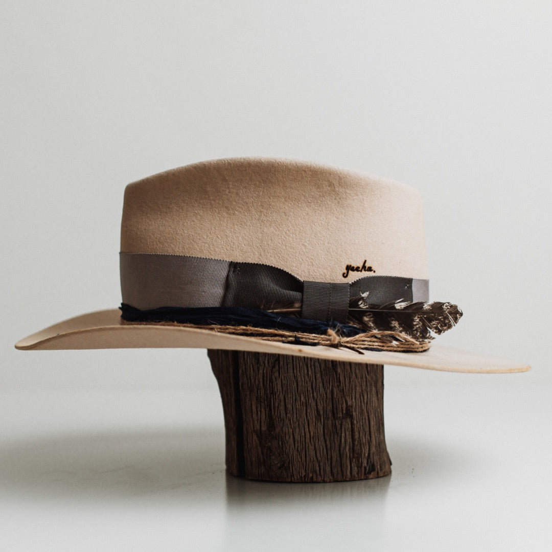 Left side view of the Wrangler beige distressed felt hat by PHYLLi Designs with royal blue sari silk trimming and twine wraps with bronze arrow charm.